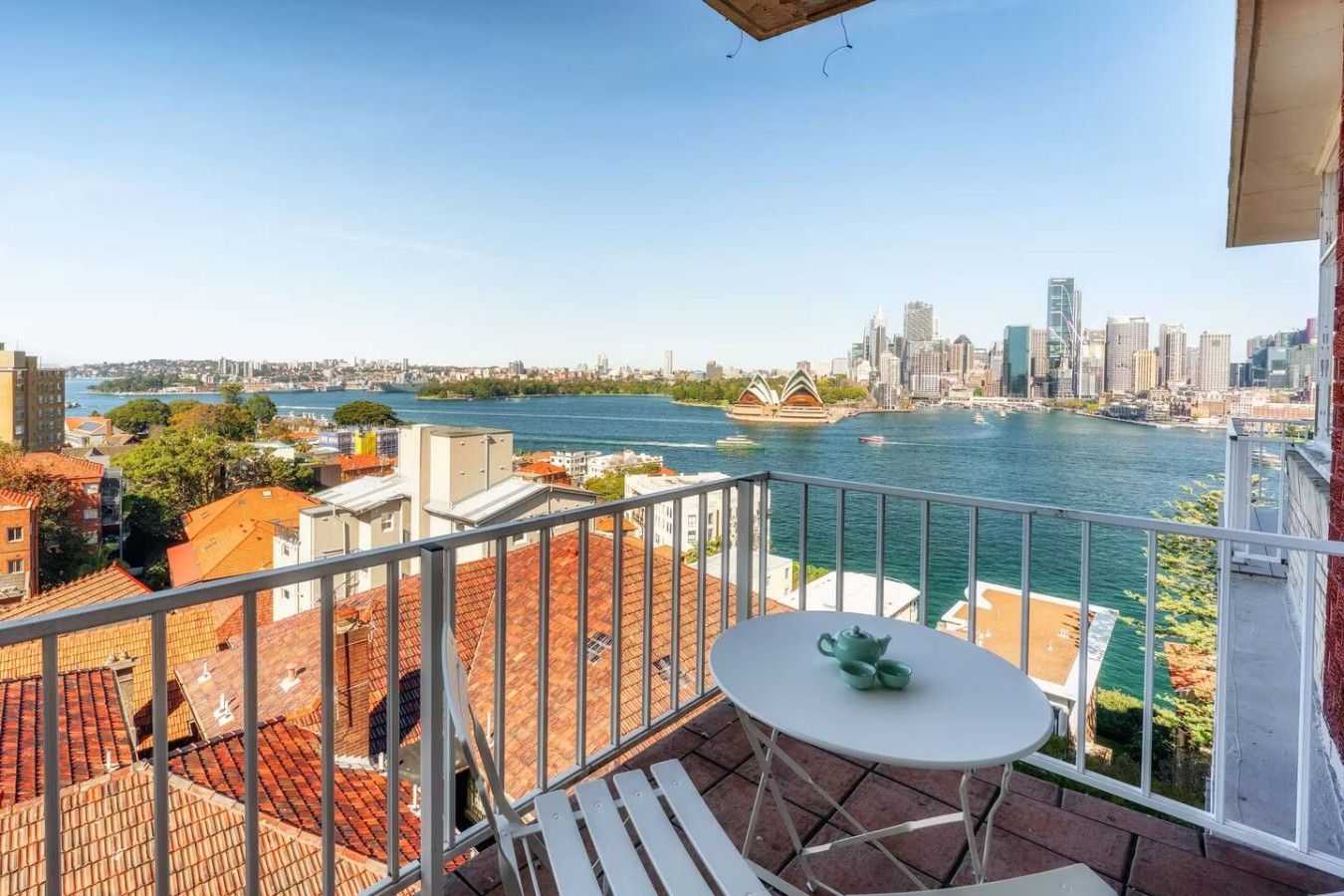 A balcony with a table and chairs, overlooking a river and city skyline.