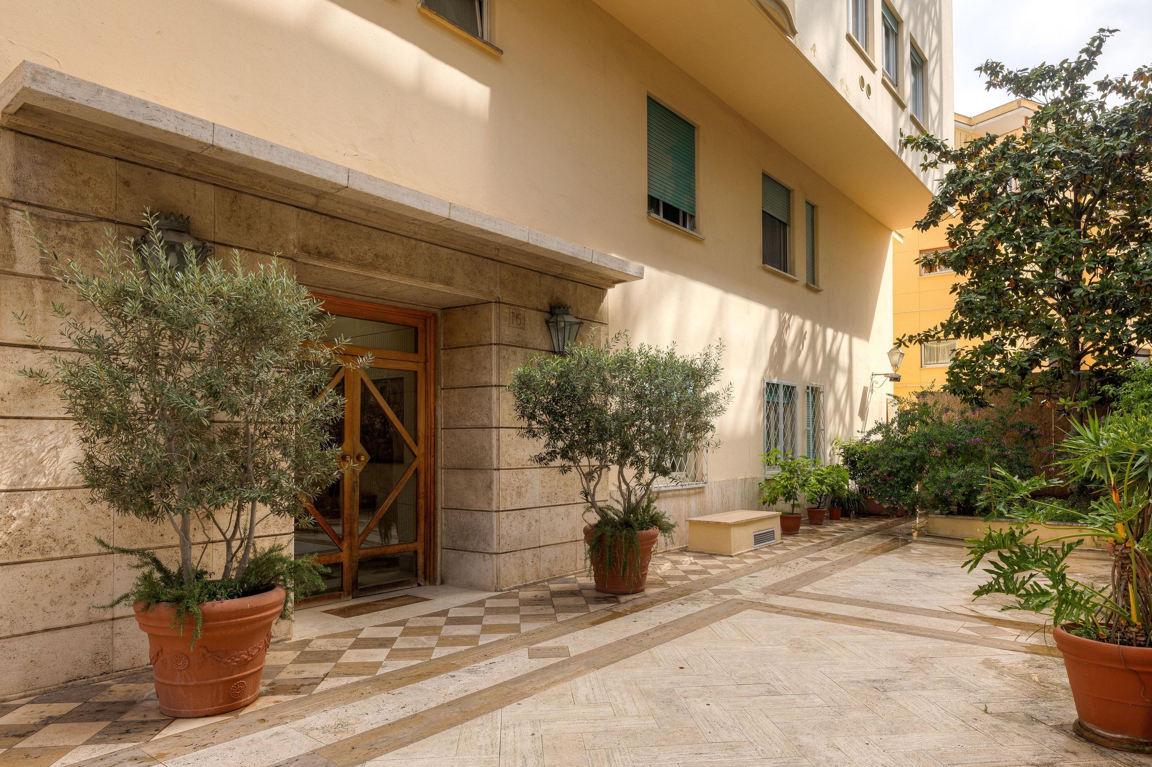 A building entrance with a checkered floor, potted plants, and a door with a glass panel.