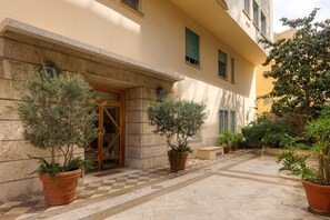 A building entrance with a checkered floor, potted plants, and a door with a glass panel. - New Listing (Roma)