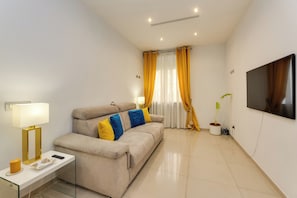 A modern living room with a sofa, a flat-screen TV, a lamp, and a potted plant. - New Listing (Roma)
