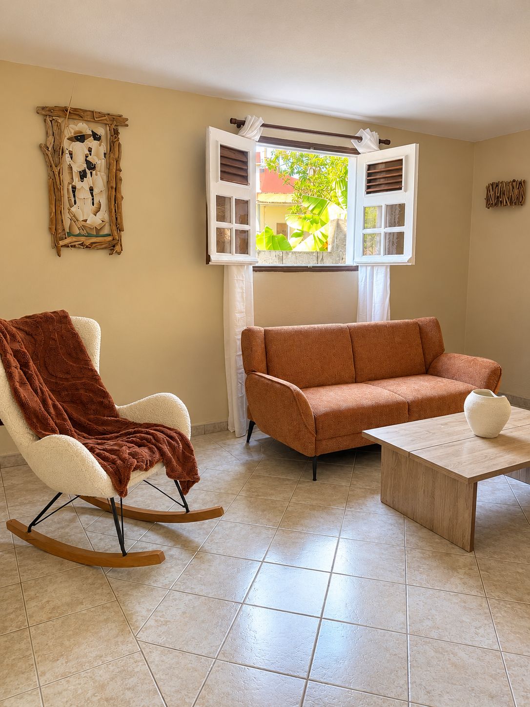 A room with a rocking chair, a sofa, and a coffee table. There is a window with curtains and a view of greenery outside.