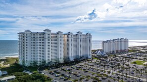 A high-rise hotel with multiple floors, a parking lot, and a view of the ocean. - Beachfront Resort Condo With Pools, Spa, Club House and Pickleball Court (Gulf Shores)