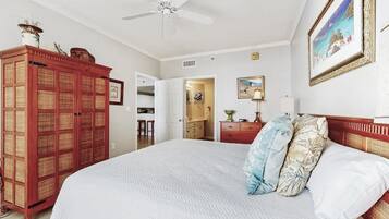 A bedroom with a large bed, a wardrobe, a ceiling fan, and a painting on the wall.