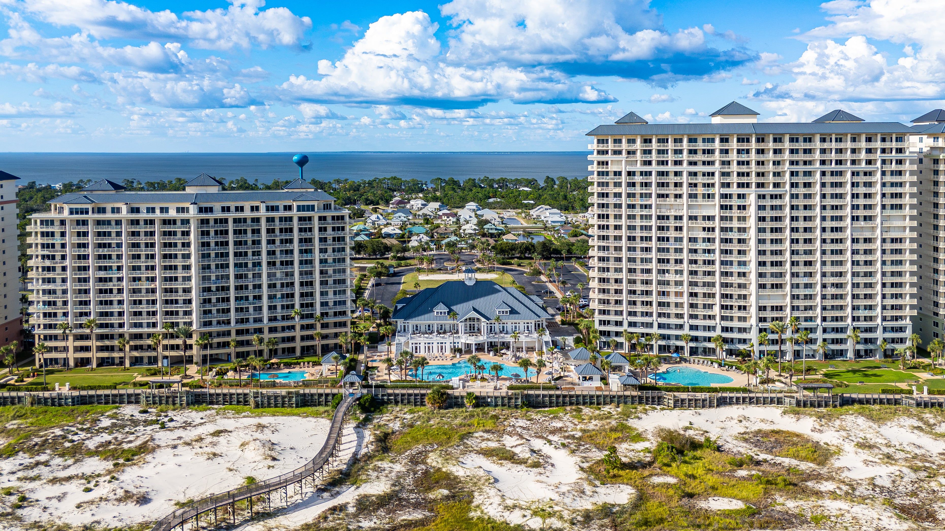 A resort with multiple high-rise buildings, a central pool area, and a beach in the foreground.
