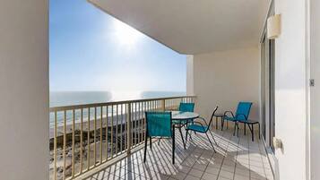 A balcony with a view of the sea, a table with chairs, and a railing.