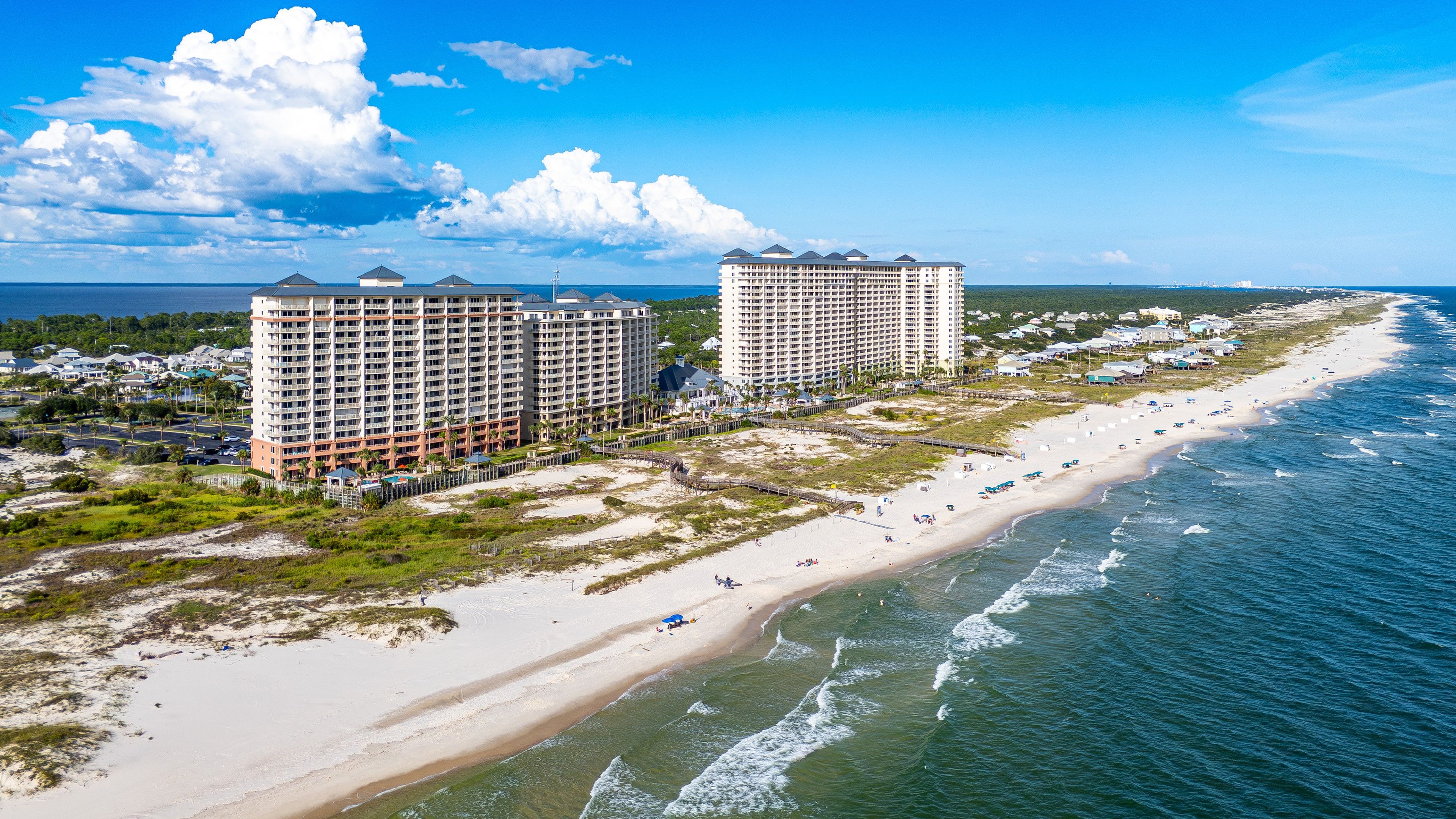 A coastal hotel with multiple high-rise buildings, a sandy beach, and a clear view of the ocean.