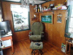 A room with a wooden floor, a green armchair, a television, and a window with a view of the outside. - Lovers Lane Getaway (Wellington North)