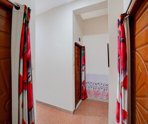A corridor with a wooden door, a tiled wall with a floral pattern, and a tiled floor. - Classic Hotel Sunshine (Gop)