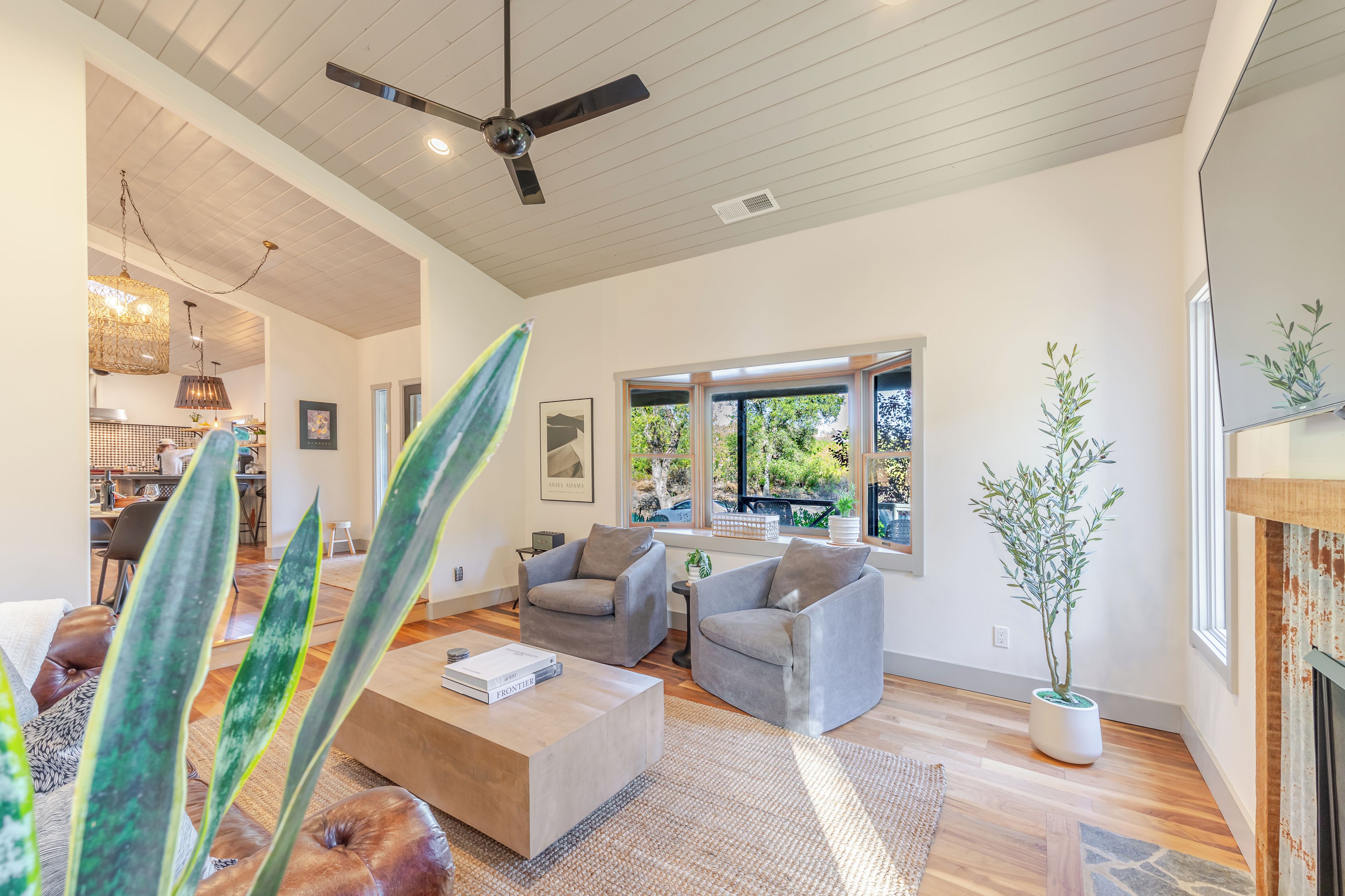 A modern living room with a ceiling fan, large windows, and a dining area visible in the background.