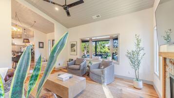 A modern living room with a ceiling fan, large windows, and a dining area visible in the background.
