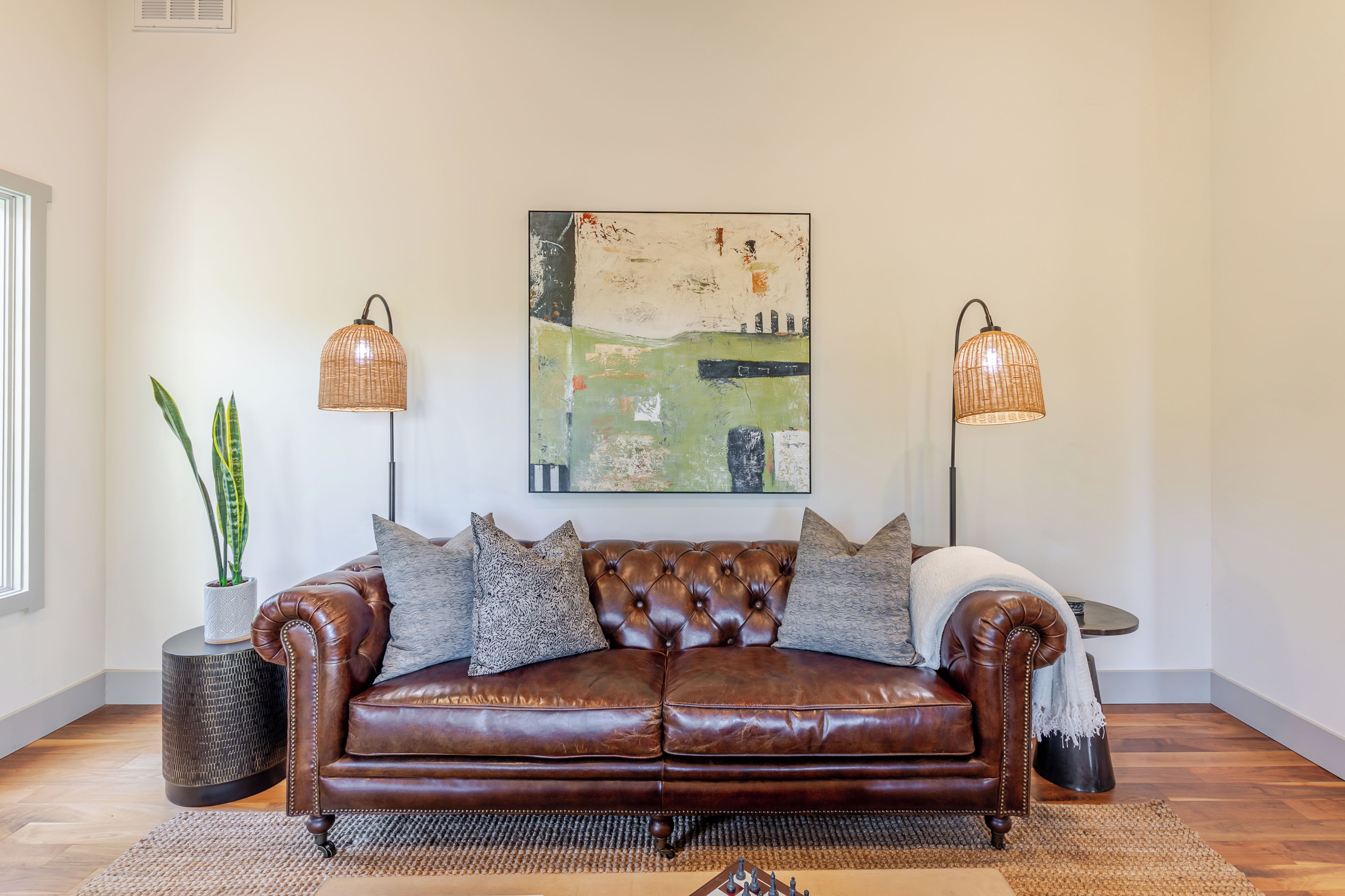A brown leather sofa with cushions, a woven rug, and two floor lamps with woven shades.
