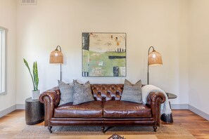 A brown leather sofa with cushions, a woven rug, and two floor lamps with woven shades. - Willow & Vine: 2 BD/2BA, BBQ, Bocce (Paso Robles)