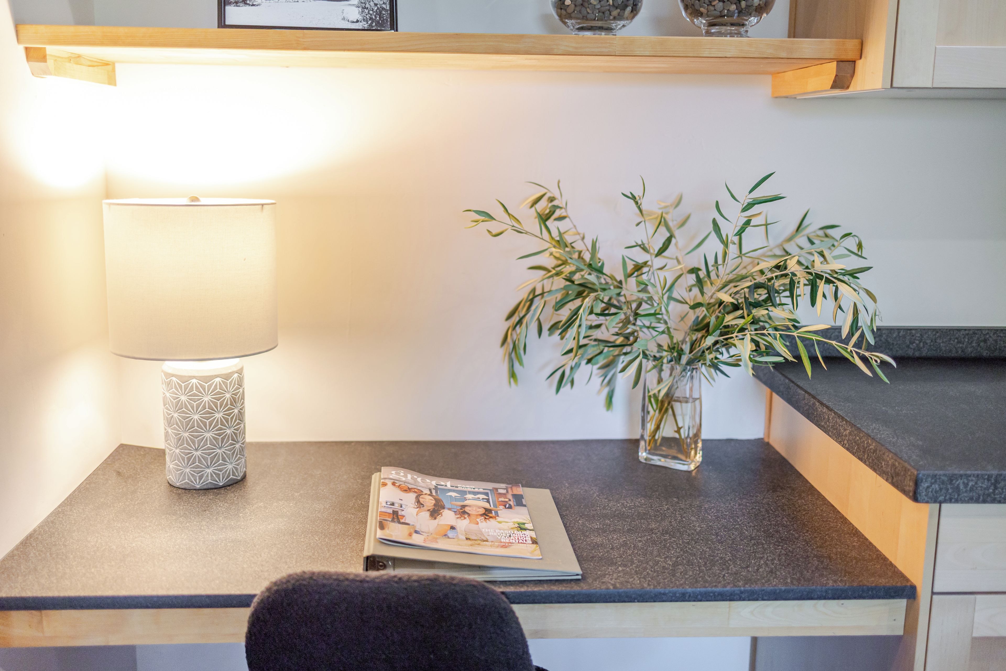 Een nachtkastje met een lamp, een klein vaasje met groene planten en een tijdschrift.