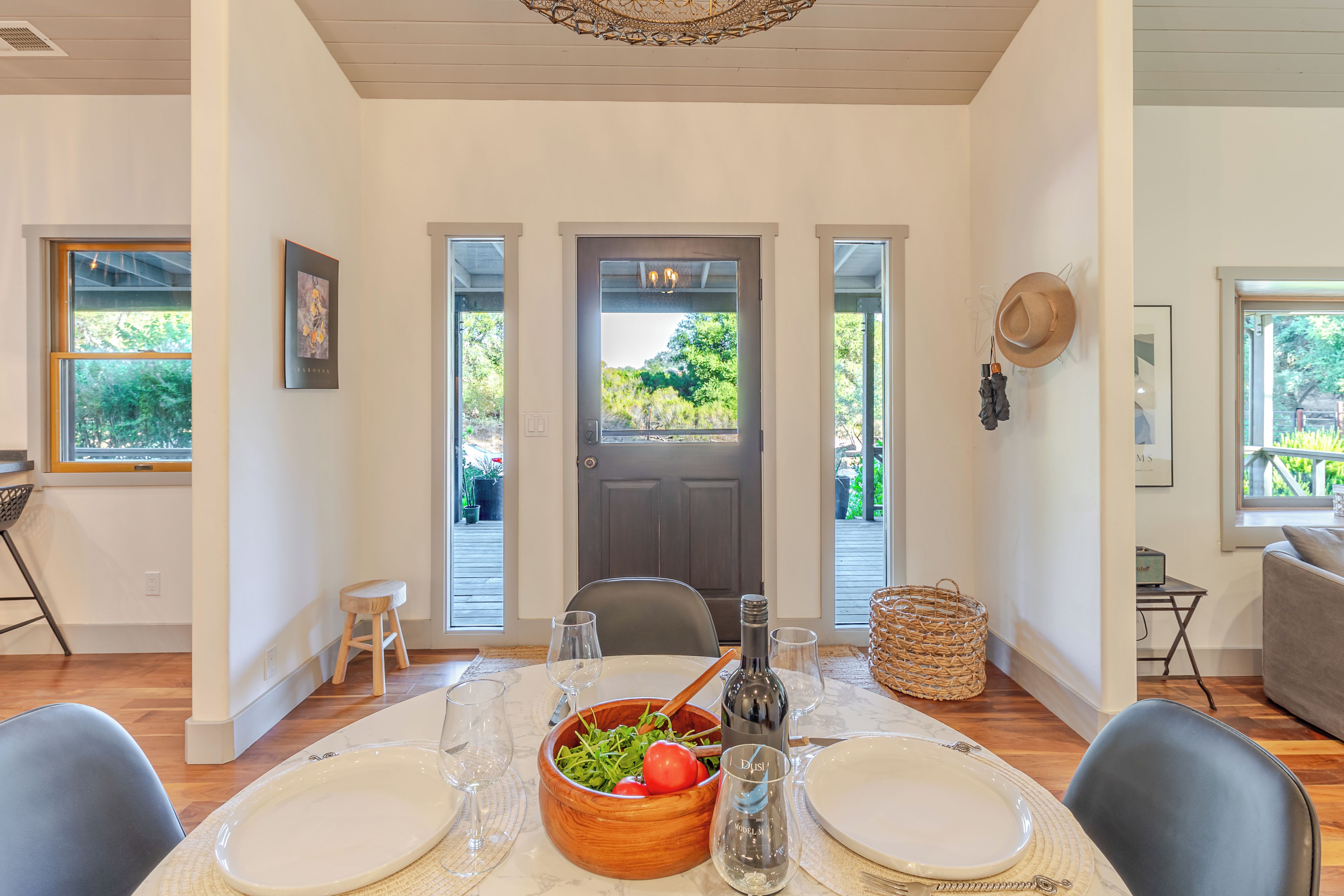 A dining area with a table set for two, a bowl of salad, wine glasses, and a bottle of wine.