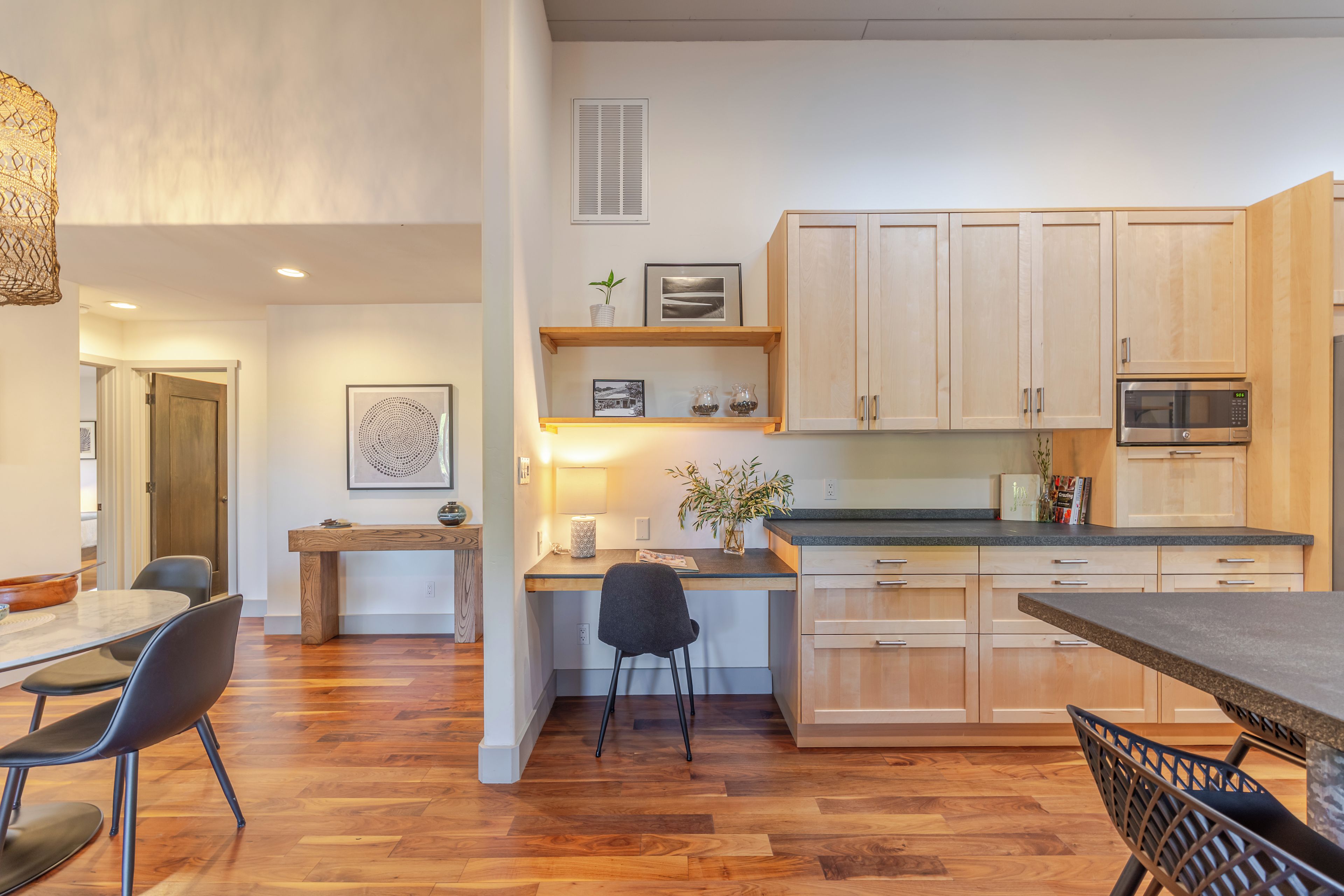 A modern kitchen with wooden cabinets, a built-in microwave, and a dining area with a table and chairs.