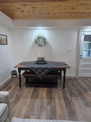A dining area with a wooden table, bench, and a wreath on the wall. - Peaceful mountain cottage near Massanutten, JMU, National Park & Shenandoah Rive (Elkton)