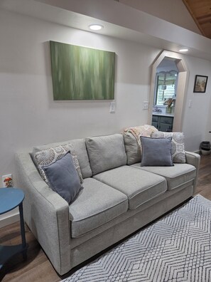 Een woonkamer met een grijze bank, gekleurde kussens, een abstract schilderij in groentinten en een vloerkleed met dessin.