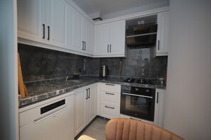 A modern kitchen with white cabinetry, a built-in oven, and a stainless steel range hood. - Serene 1-bedroom condo in Samsun perfect for a relaxing getaway (Samsun)