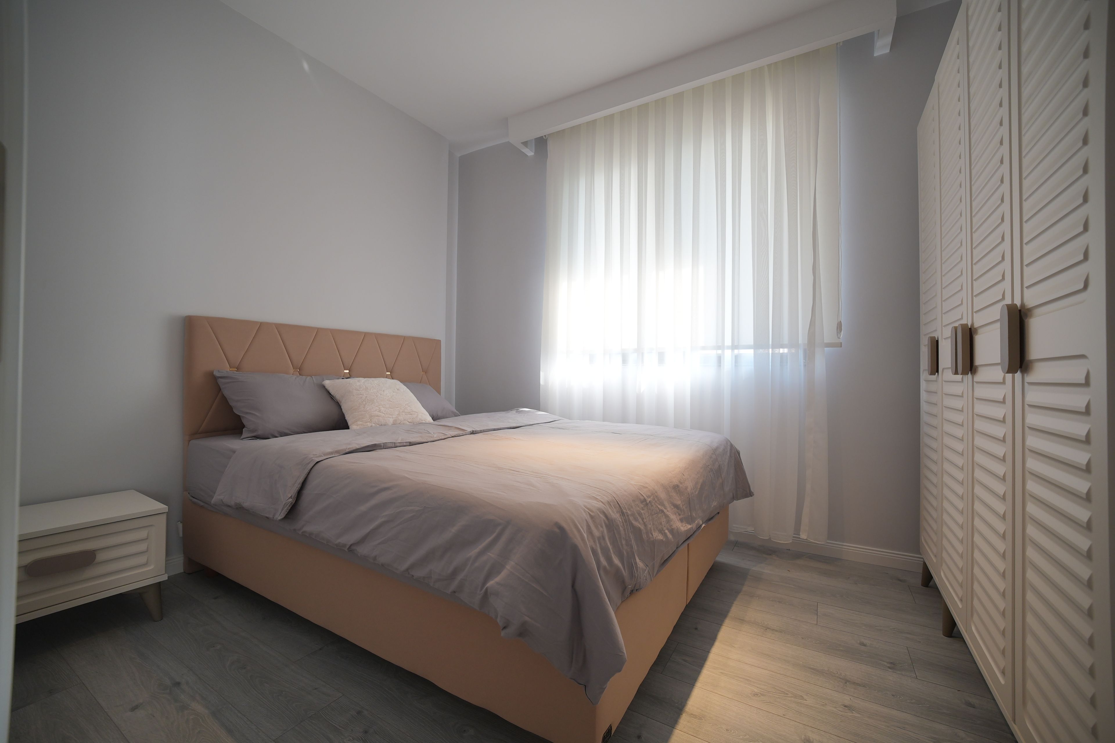 A bedroom with a bed, a nightstand, a wardrobe, and a window with curtains.