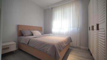 A bedroom with a bed, a nightstand, a wardrobe, and a window with curtains.