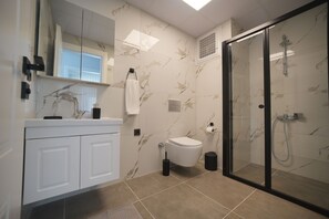 A modern bathroom with a glass shower enclosure, a toilet, and a vanity with a mirror. - Serene 1-bedroom condo in Samsun perfect for a relaxing getaway (Samsun)
