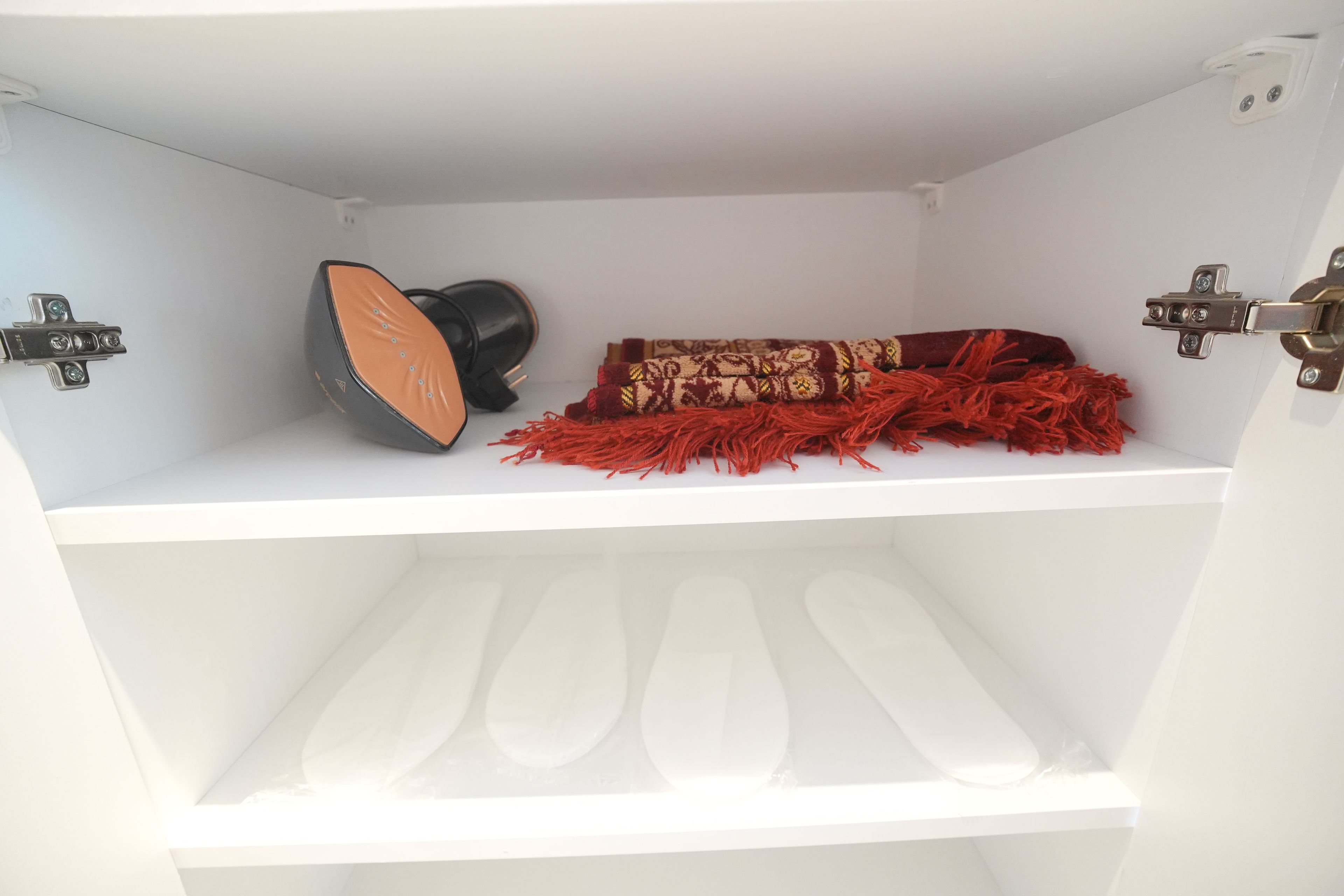A white shelf with a black object, a patterned fabric, and a red fringe item.