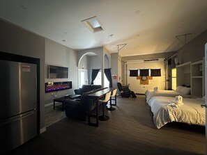 A modern hotel room with a flat-screen TV, a fireplace, a dining area with a table and chairs, and two beds. - Modern Coach House (Cochrane)
