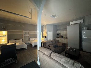 A hotel room with a bed, a sofa, a desk, and a kitchenette. - Modern Coach House (Cochrane)