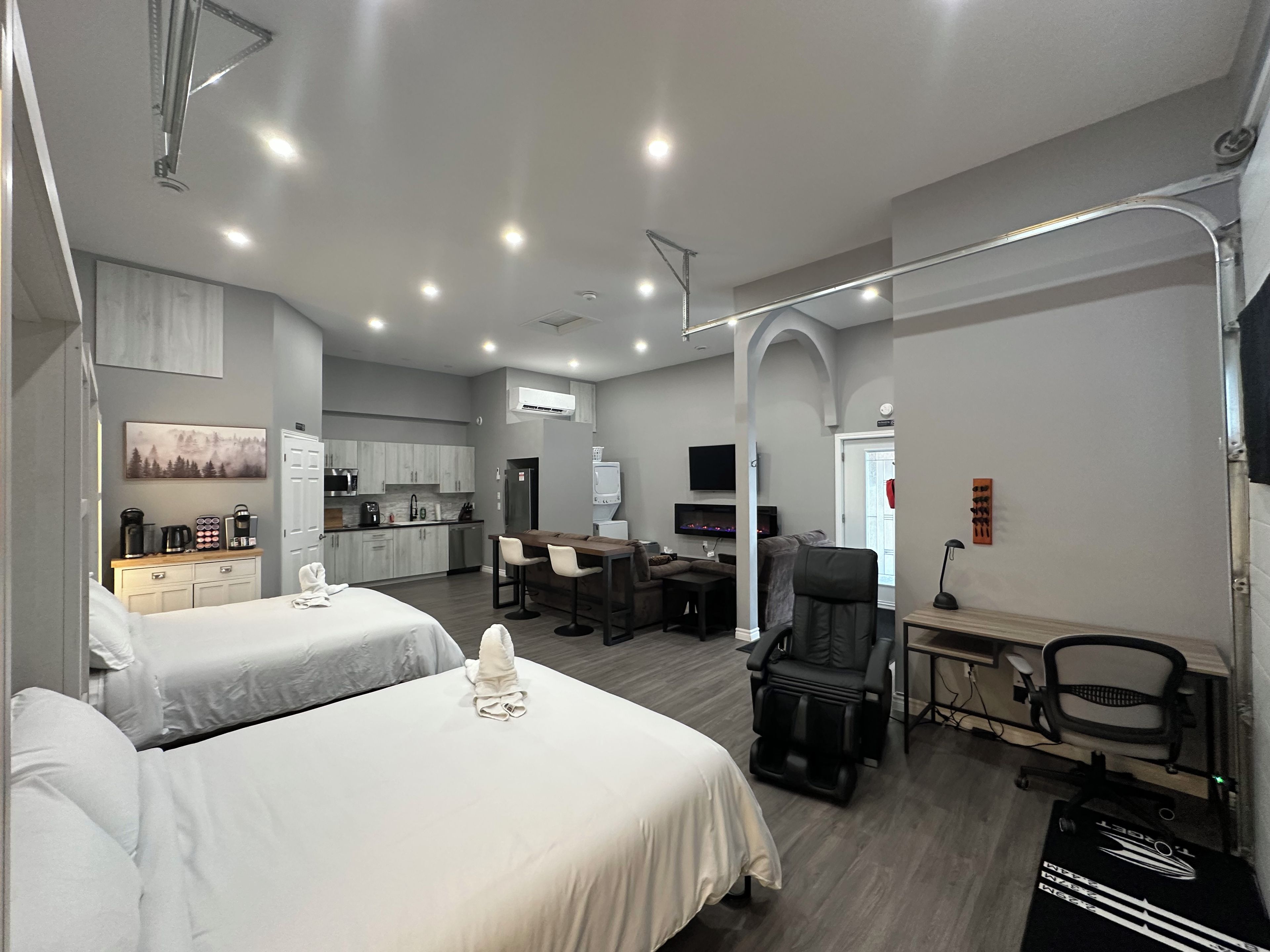 Quarto de hotel com duas camas, cozinha compacta, área de refeições e cadeira de massagem.