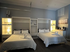 A hotel room with two beds, bedside tables with lamps, a wardrobe, a coffee machine, and a painting on the wall.
