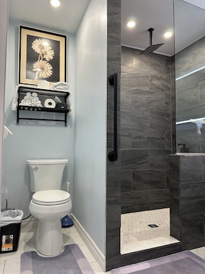 A modern bathroom with a toilet, a shower with a glass door, and a towel rack with towels. - Modern Coach House (Cochrane)