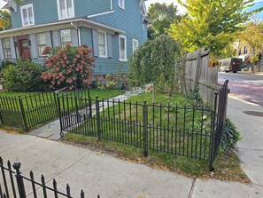 Een woonstraat met huizen, een zwart metalen hek en een kleine tuin.