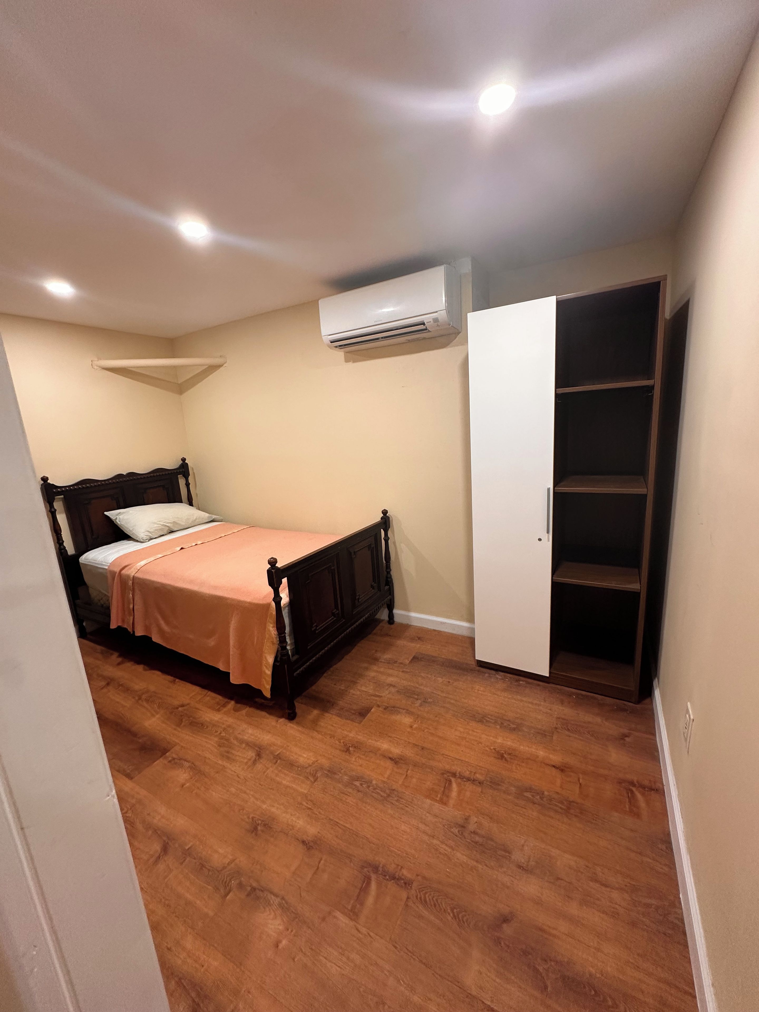 A bedroom with a bed, an air conditioning unit, a wardrobe, and wooden flooring.