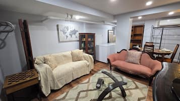 Uma sala de estar com sofá, mesa de centro de vidro, mesa de xadrez e uma área de jantar com cadeiras e mesa.