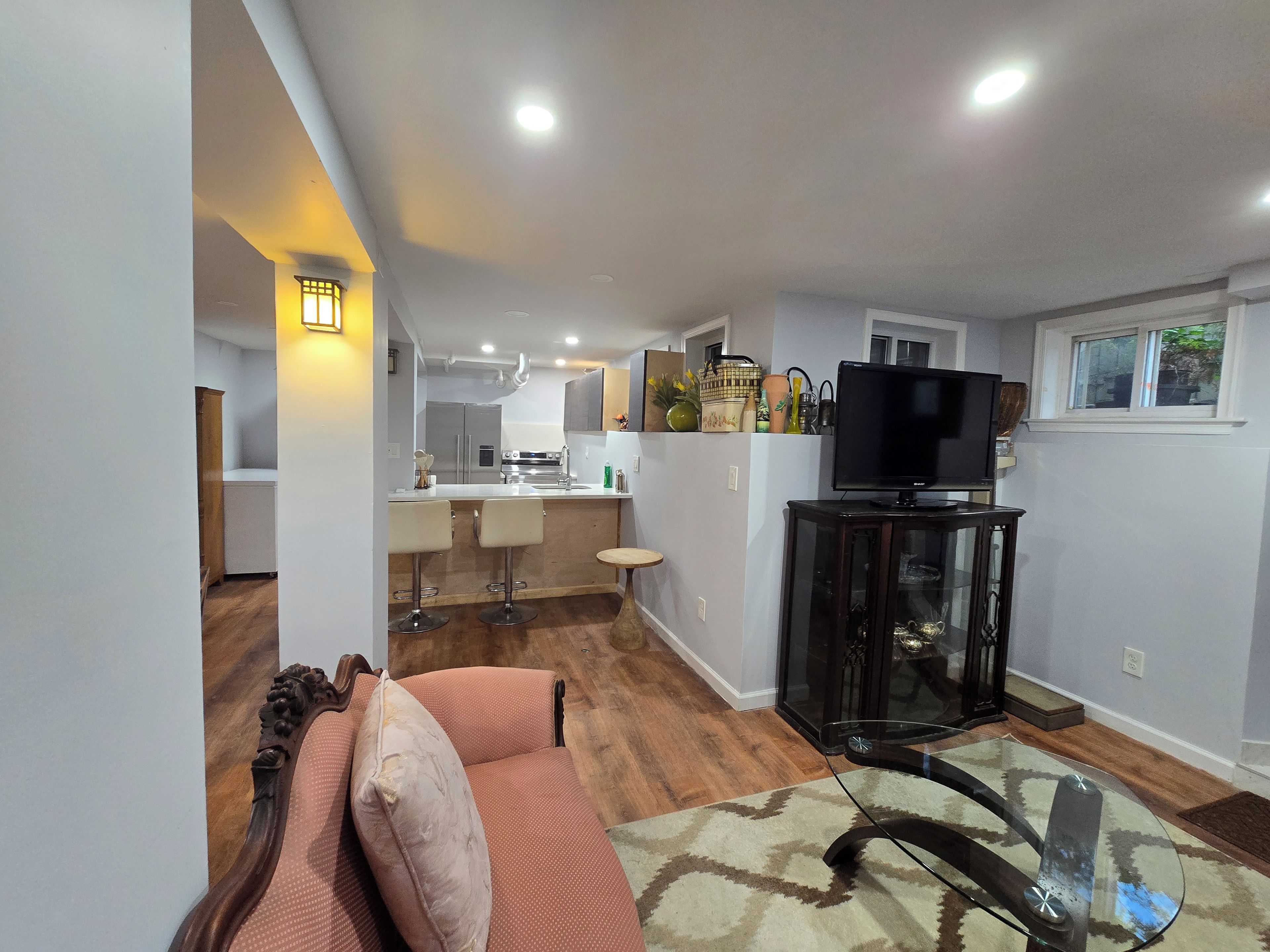 Una sala moderna con una mesa de centro de vidrio, un sofá con cojines y un televisor sobre un mueble.