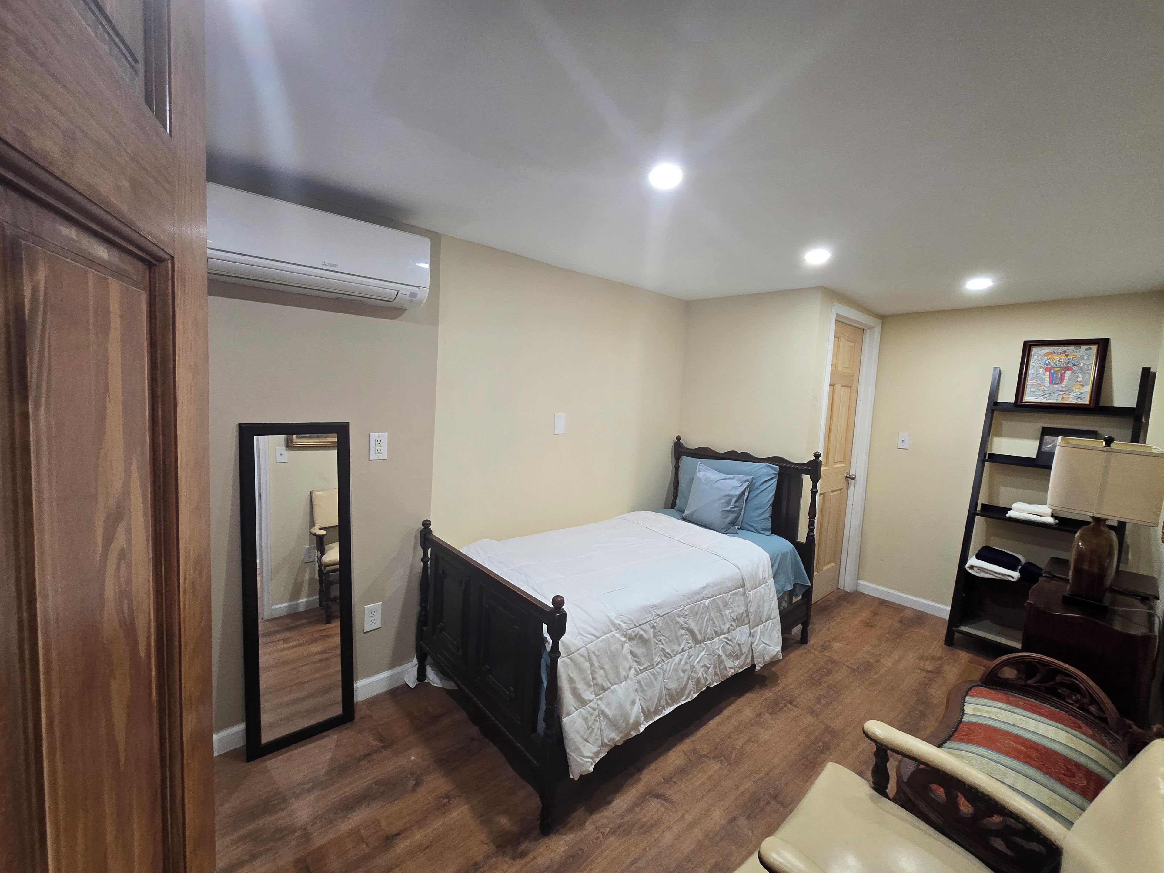 Quarto com cama, poltrona, guarda-roupa e espelho.