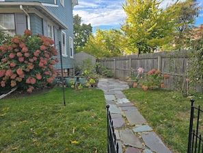 A stone pathway leading to a house with a wooden fence and flowering bushes. - Historical 2BR APT in Brooklyn NY (Brooklyn)