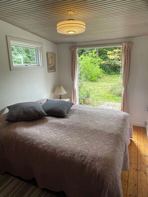 A bedroom with a large bed, a bedside lamp, a window, and a view of greenery outside. - Lovely holiday home near the beach (Asnæs)