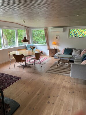 A modern living room with a dining area, large windows, and a view of greenery. - Lovely holiday home near the beach (Asnæs)