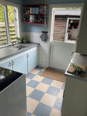 A kitchen with a checkered floor, a sink, cabinets, and a window with a view of greenery. - Lovely holiday home near the beach (Asnæs)