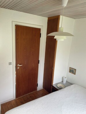 A room with a wooden door, a white textured wall, a white ceiling, and a white bed. - Lovely holiday home near the beach (Asnæs)