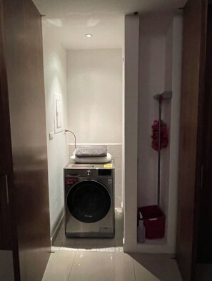A laundry room with a washing machine, a small red trash bin, and a floor lamp. - Depto 204 (Ciudad de México)