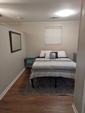 A bedroom with a bed, a bedside table, a mirror, a window with blinds, and a ceiling light. - Cozy Flat, Super Central Location (Pensacola)