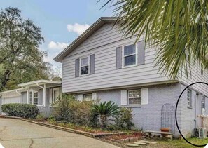 A two-story house with a porch, a small garden, and a visible garage. - Cozy Flat, Super Central Location (Pensacola)