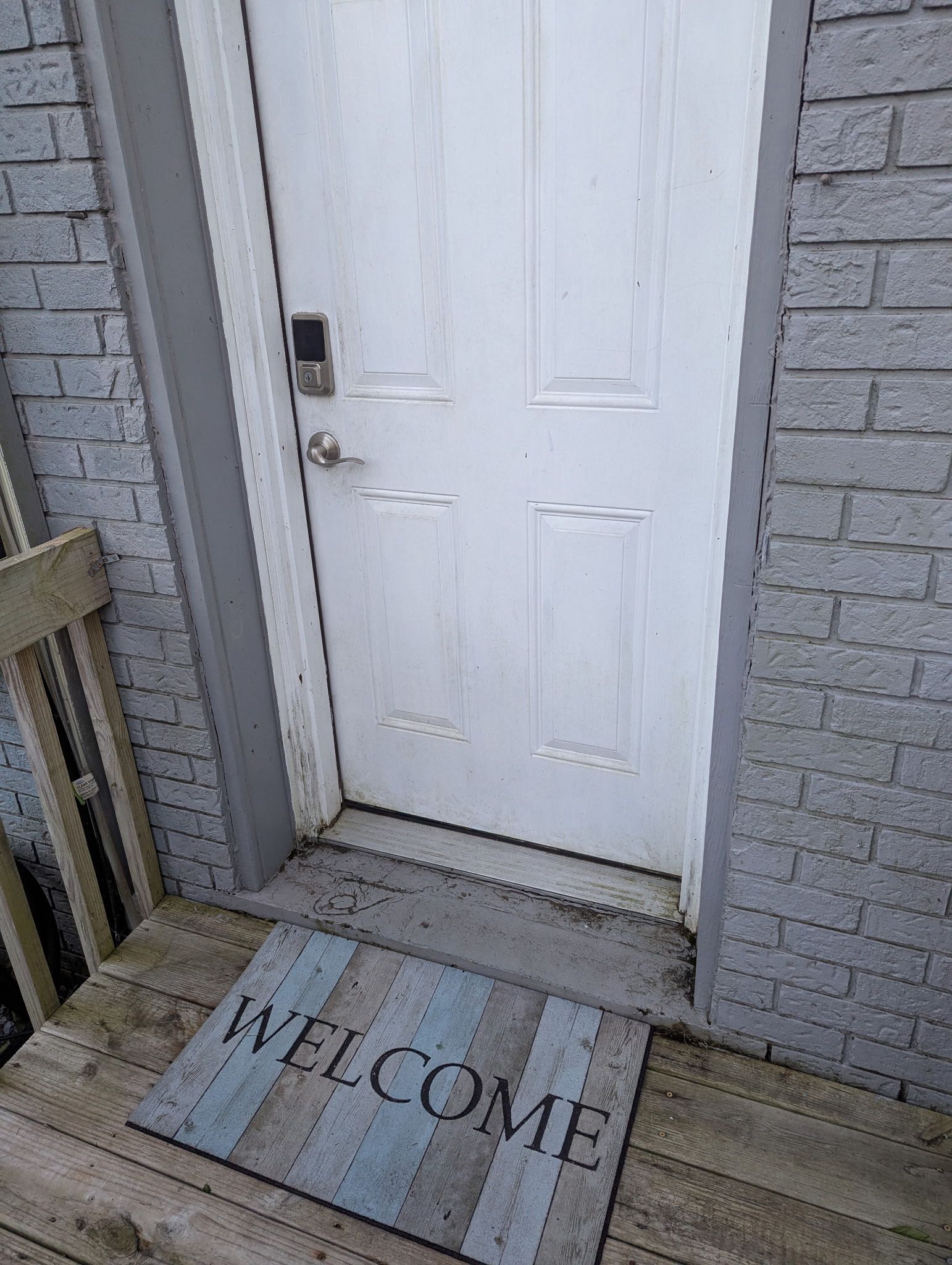 A white door with a keypad lock, a wooden bench, and a welcome mat.