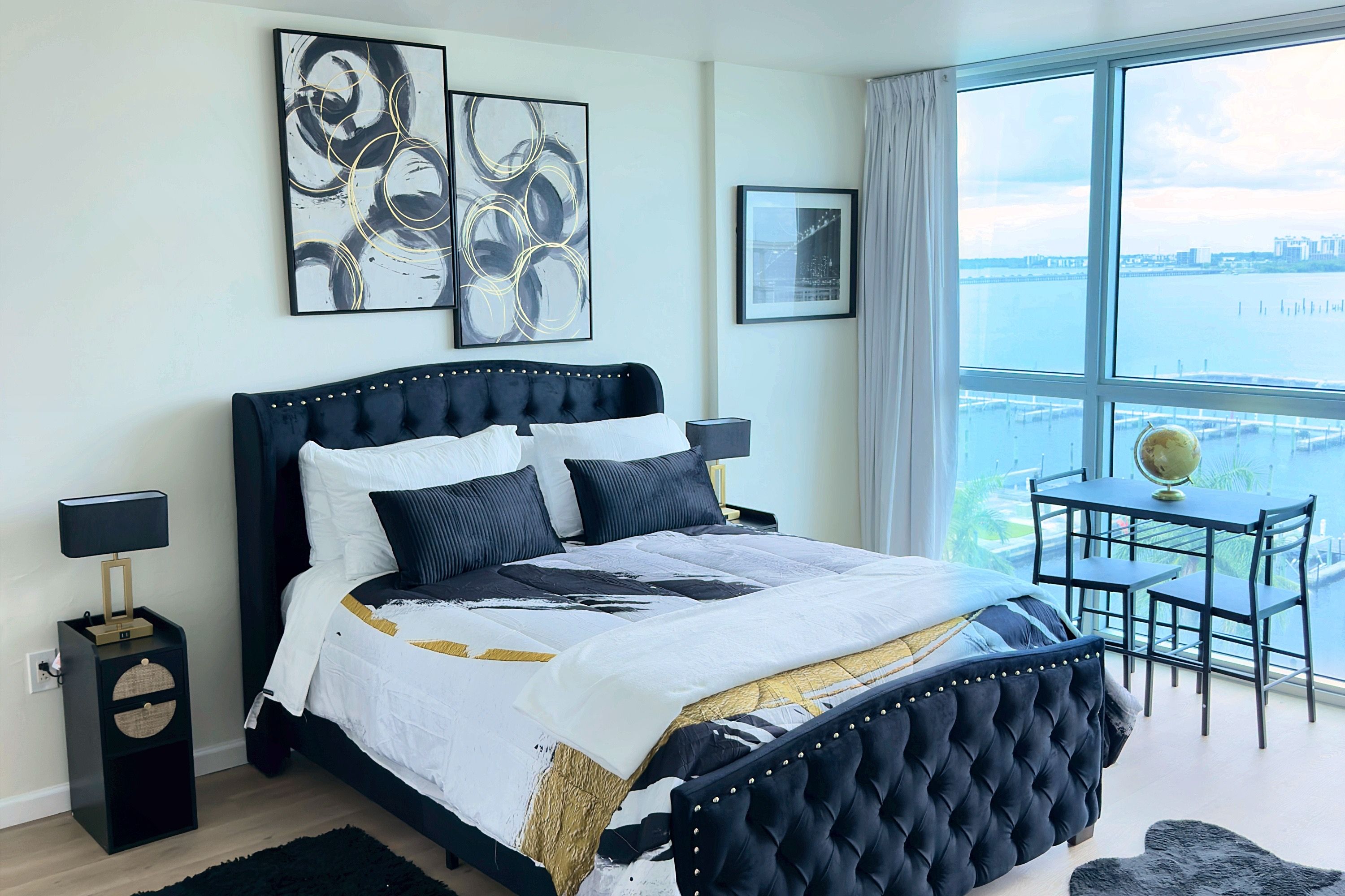 Een slaapkamer met een groot bed, een nachtkastje, een stoel en uitzicht op de stad door een raam.