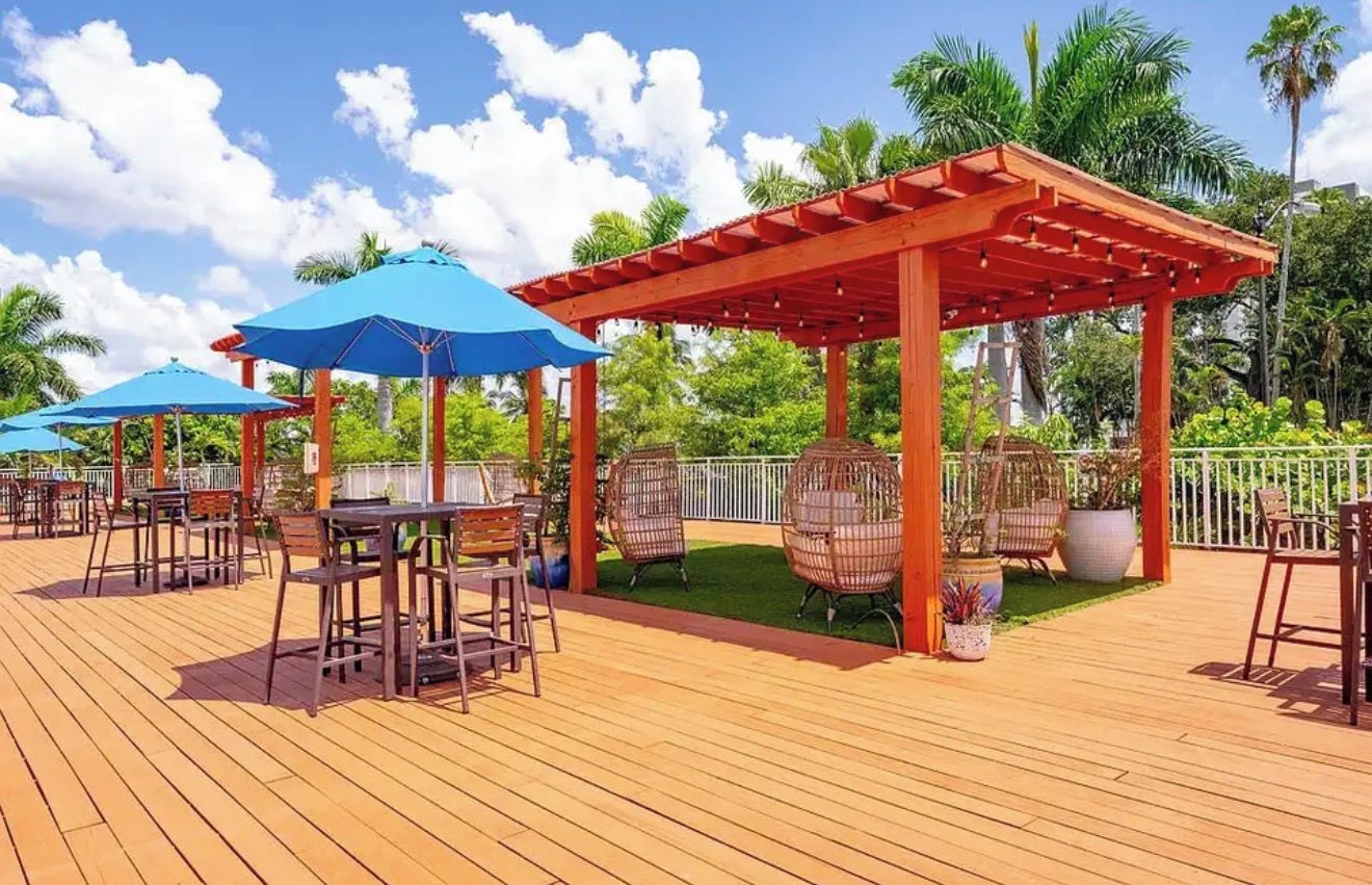 An outdoor deck with wooden flooring, tables, chairs, and blue umbrellas.
