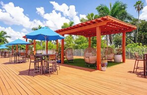 Een terras buiten met houten vloer, tafels, stoelen en blauwe parasols.