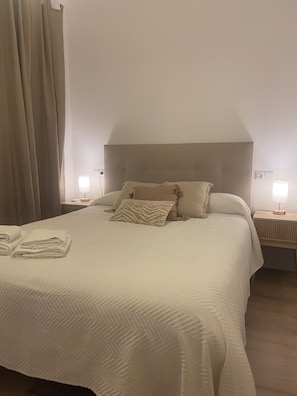 Ein ordentlich bezogenes Bett mit Kopfteil, zwei Nachttischlampen und ein Paar gefaltete Handtücher auf dem Bett.