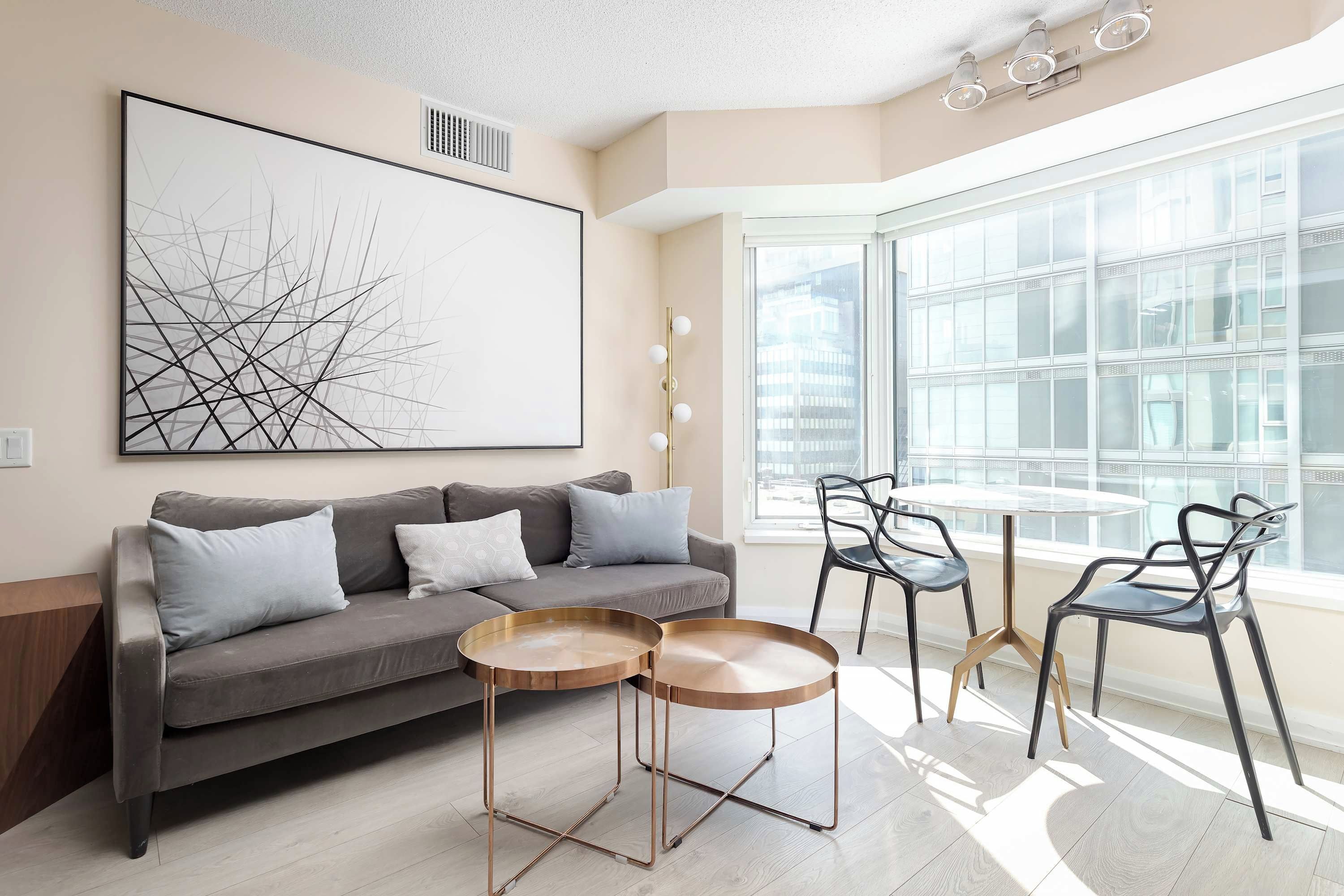 A modern living room with a grey sofa, two round coffee tables, and a large window with a city view.